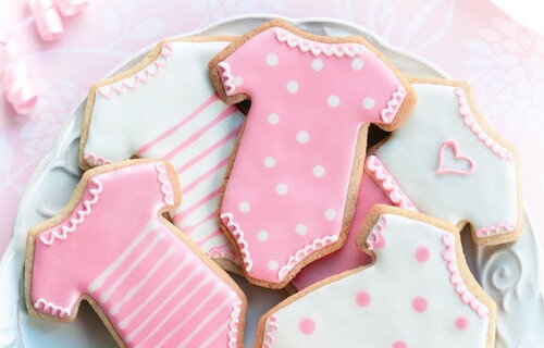 A close up of some decorated biscuits in the shape of baby playsuits, in pink and white with spots and stripes