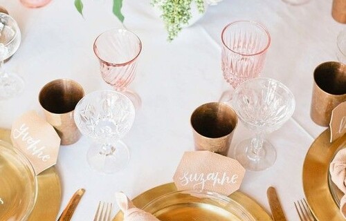 A close up of a table set for dinner, with gold plates, pink napkins and glasses and a floral arrangement as a centrepiece
