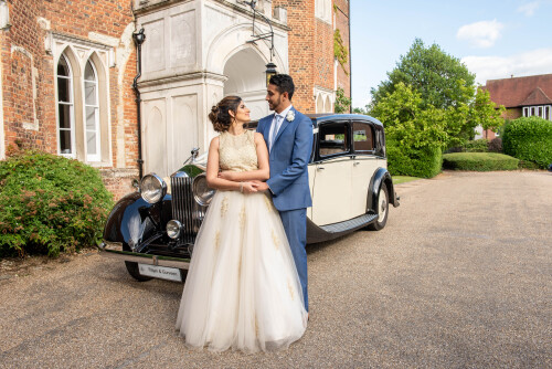 A bride and groom stood in front of a black and white car parked outside Hertford Castle