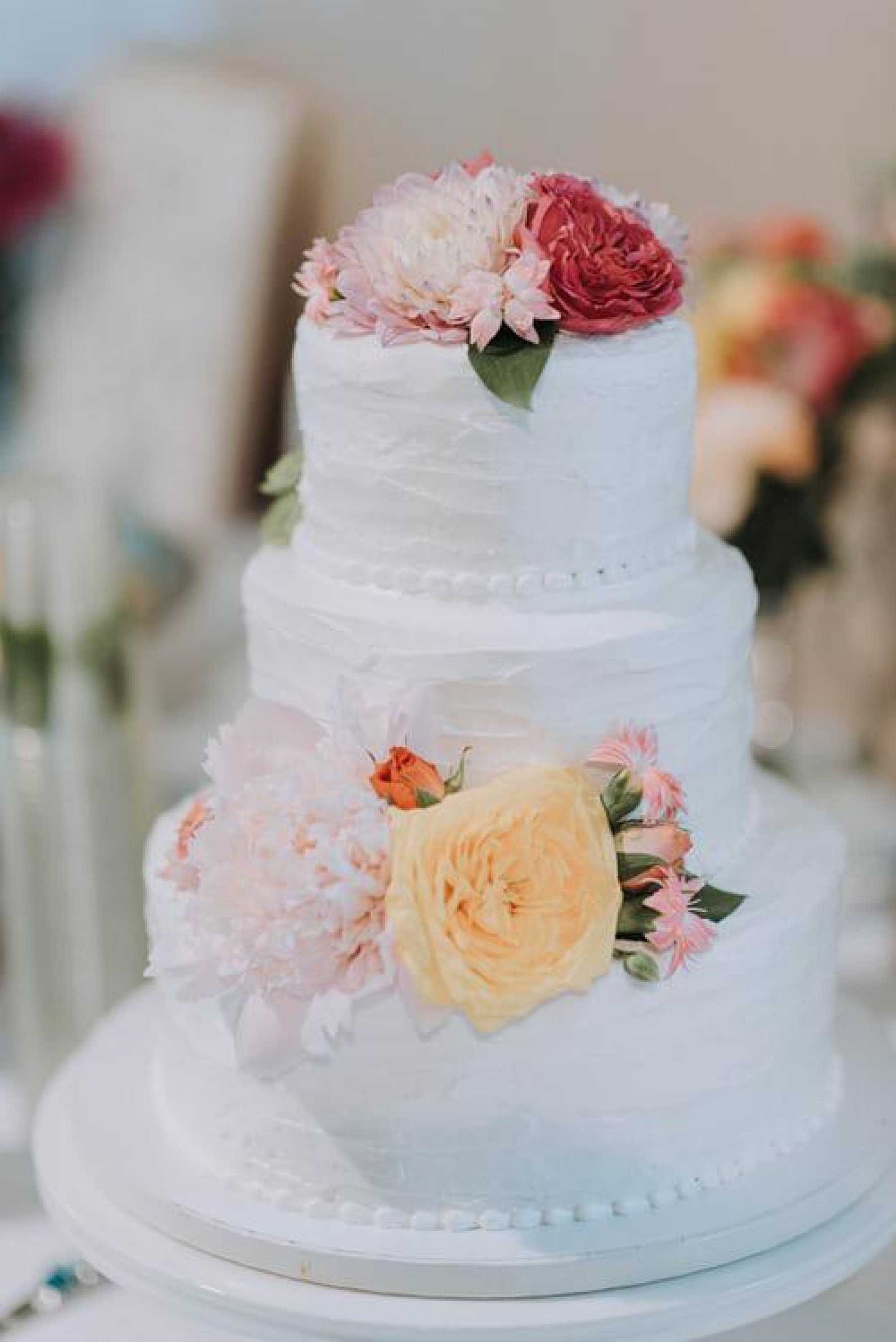 A close up of a wedding cake with pink, yellow and red flowers on it
