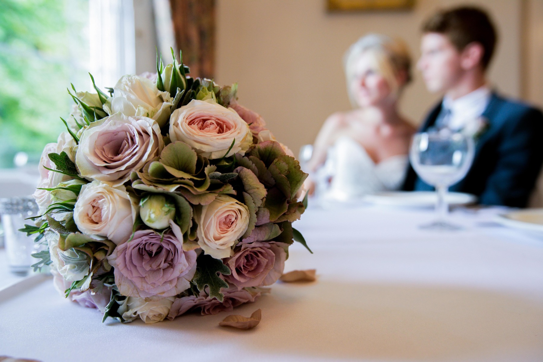 close up of a bouquet of dusky pink flower, a bride and groom blurred in the background