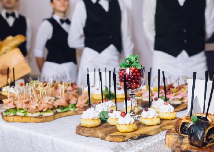 A close up of a table, with waiters in the background, covered in canapes and other food bits