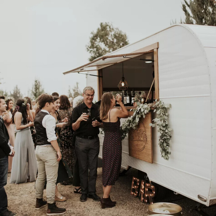 Guests queuing outside a converted horse trailer that is now a bar, laughing and holding drinks