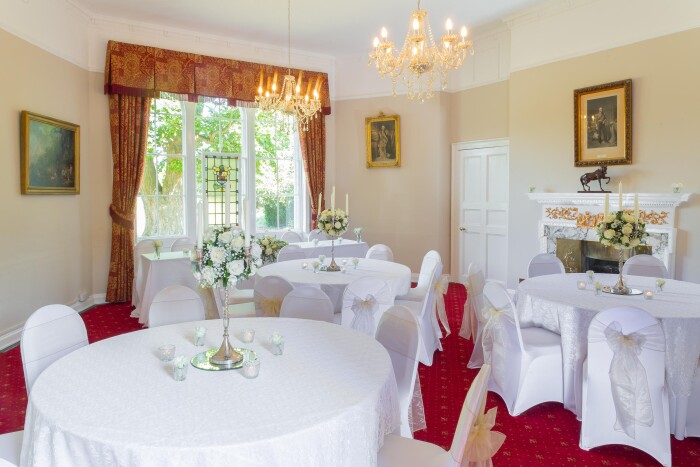 The Salisbury room set up for a reception with white table cloths on round tables, chairs in white covers with yellow bows