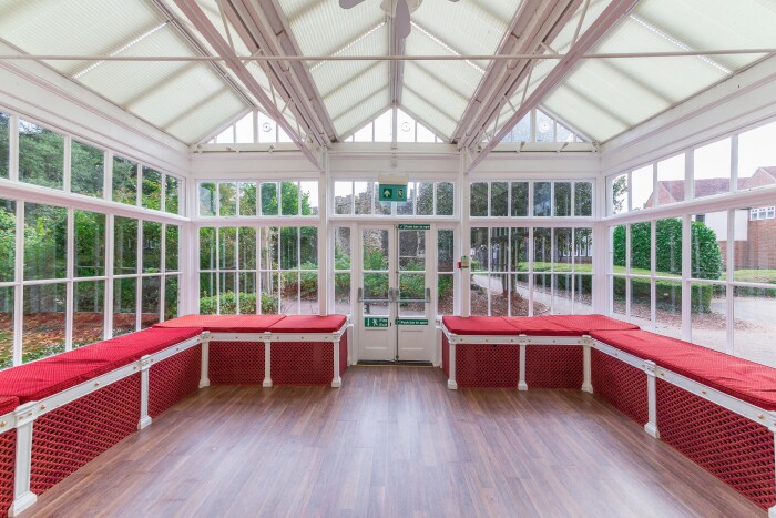 The Conservatory with white metal frame and glass looking out over the main lawn, the red cushioned benches around the edges