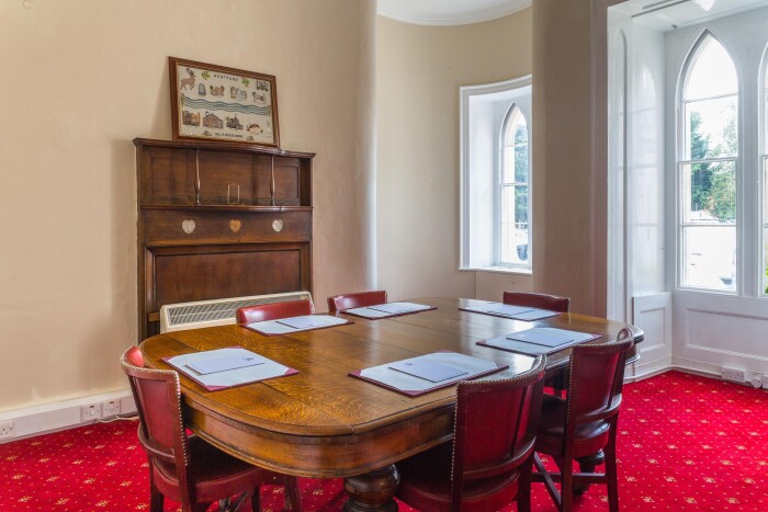 The Cecil Room set up for a meeting with a wooden table and chairs in the centre of the room, a wooden back fireplace on the back wall. 