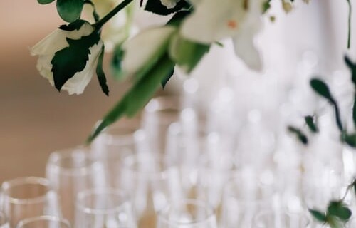 a close up shot of champagne flutes lined up on a table with flowers in the foreground