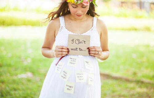 A shot of a expecting mother dressed in white, holding a sign that says