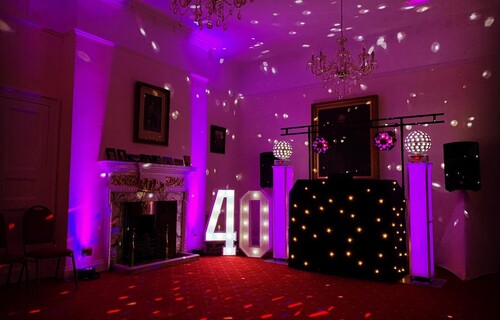 The Salisbury room set up with DJ with a large number 40 in lights to the side, disco balls casting light onto the ceiling and the ornate fireplace in