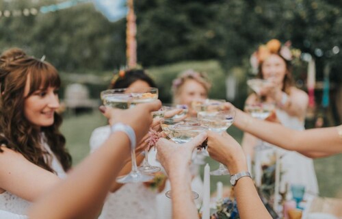 A bride and her bridal party holding champagne coupes and toasting together
