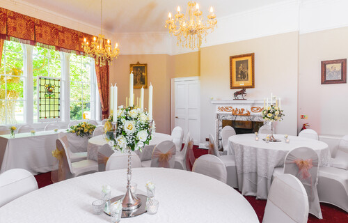 The Salisbury room set up for a reception with white table cloths on round tables, chairs in white covers with pink bows