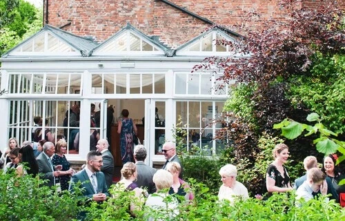 a side view of Hertford Castle showing the conservatory with guest spilling out, drinking and having fun together
