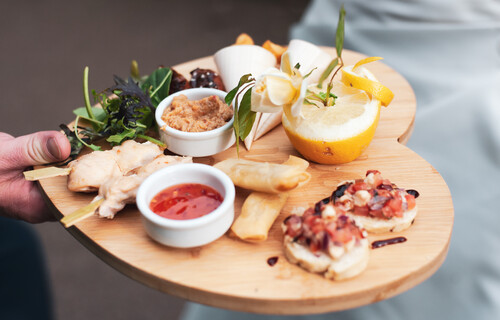 a close up of wooden heart shaped board with canapes, dips and salad on