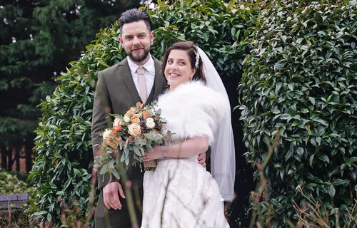 Groom with Bride holding flowers and smiling.