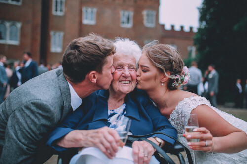 A bride and groom kissing a grandma on each cheek, Hertford Castle in the background