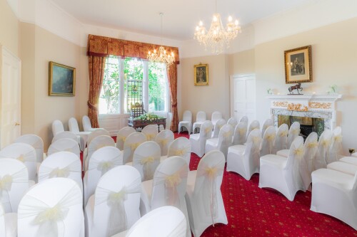 the salisbury room set up for a ceremony, rows of chairs in white covers with yellow bows facing the window with the stained glass centre