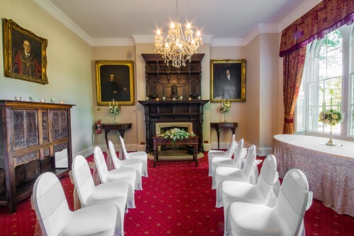 The Mayor's Parlour set up for a small wedding ceremony, the white covered chairs forming a central aisle up to the grand fireplace, paintings on the 
