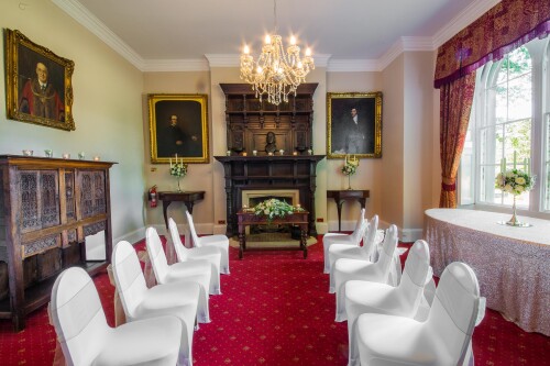 The Mayor's Parlour set up for a small wedding ceremony, the white covered chairs forming a central aisle up to the grand fireplace, paintings on the