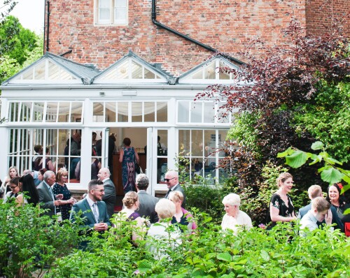 a side view of Hertford Castle showing the conservatory with guest spilling out, drinking and having fun together