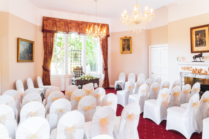 the salisbury room set up for a ceremony, rows of chairs in white covers with yellow bows facing the window with the stained glass centre