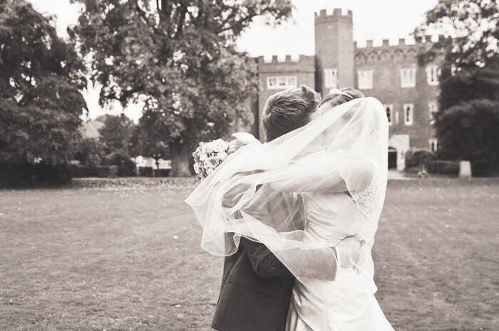 a groom kissing his bride with Hertford Castle in the background, her veil caught in the wind