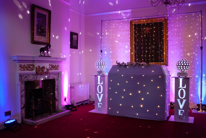 the Salisbury room set up for a party, with a DJ booth in white with twinkle lights, disco balls and letters spelling out love each side.