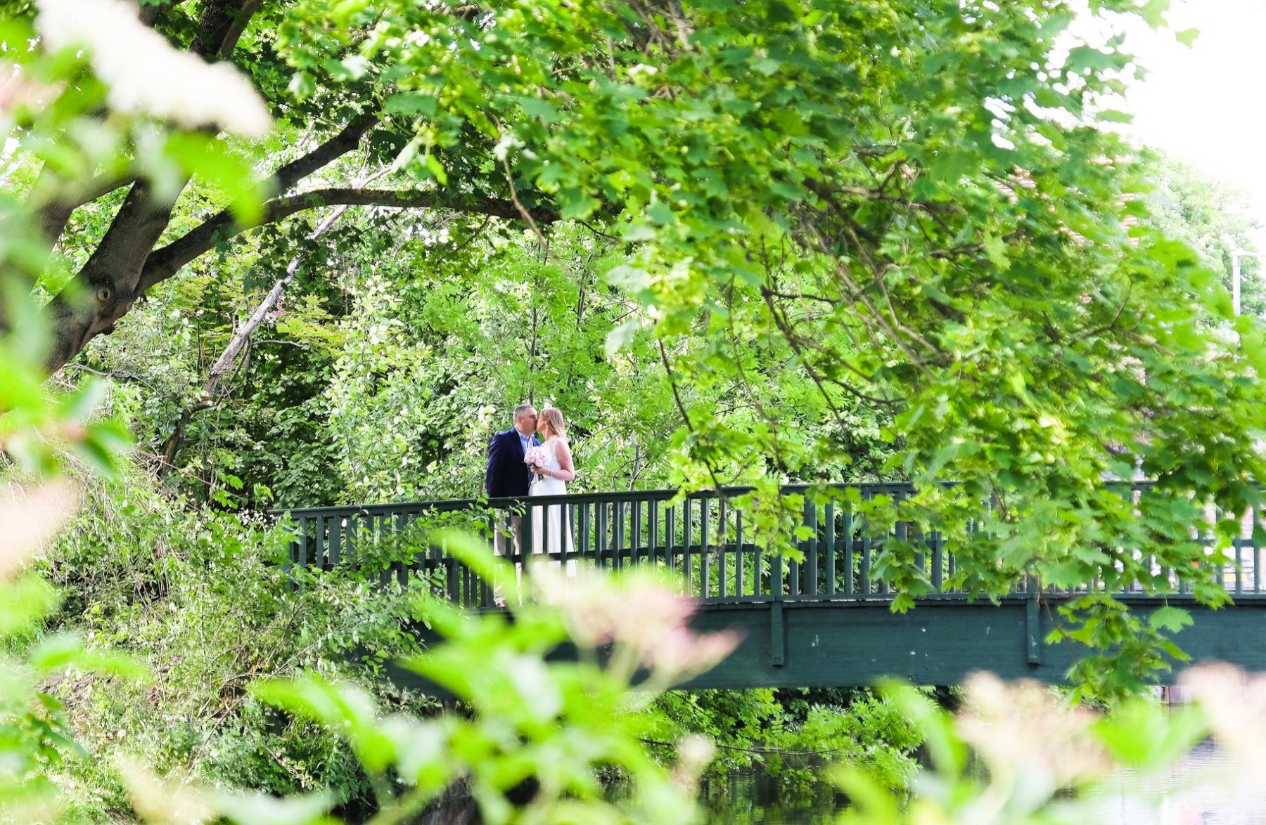 A couple kissing on the green bridge above the river lea, surrounded by green trees