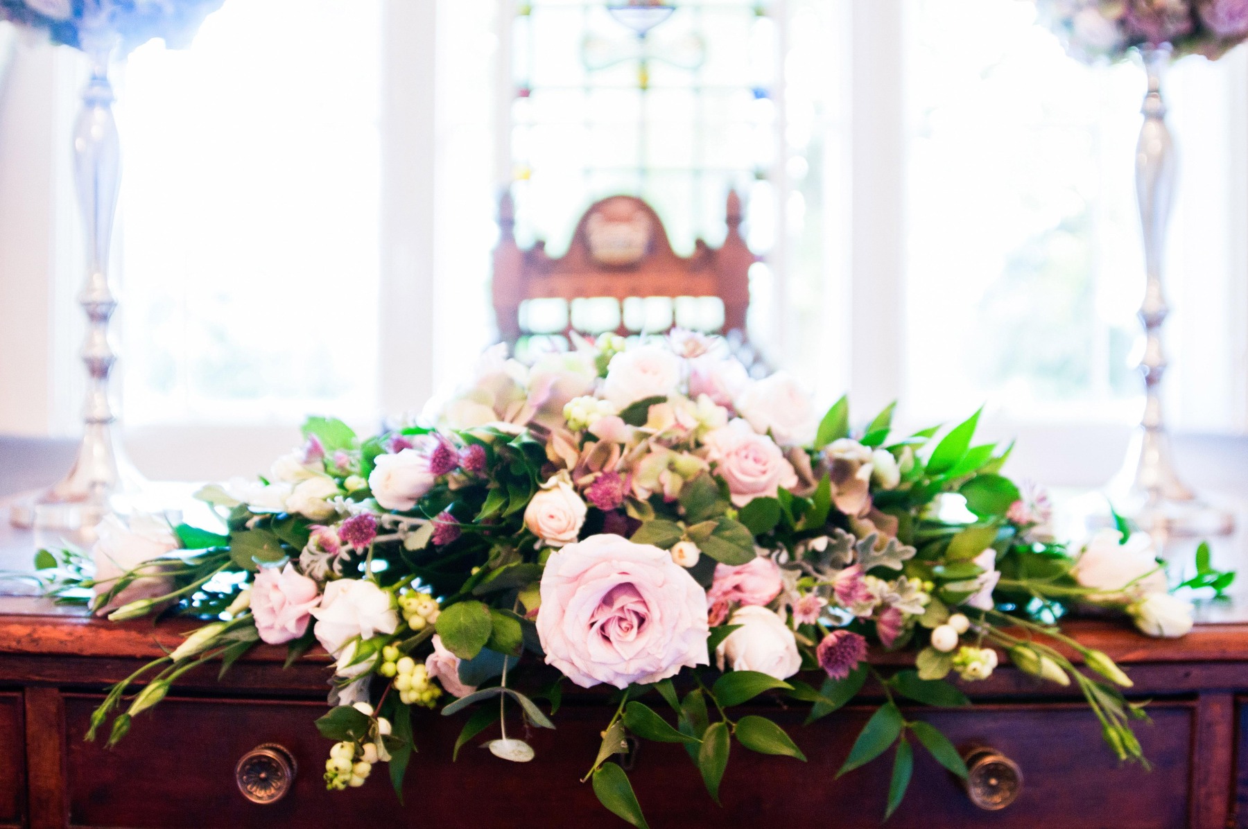 A close up of a floral display of pink flowers in front of the winged chair and stained glass window