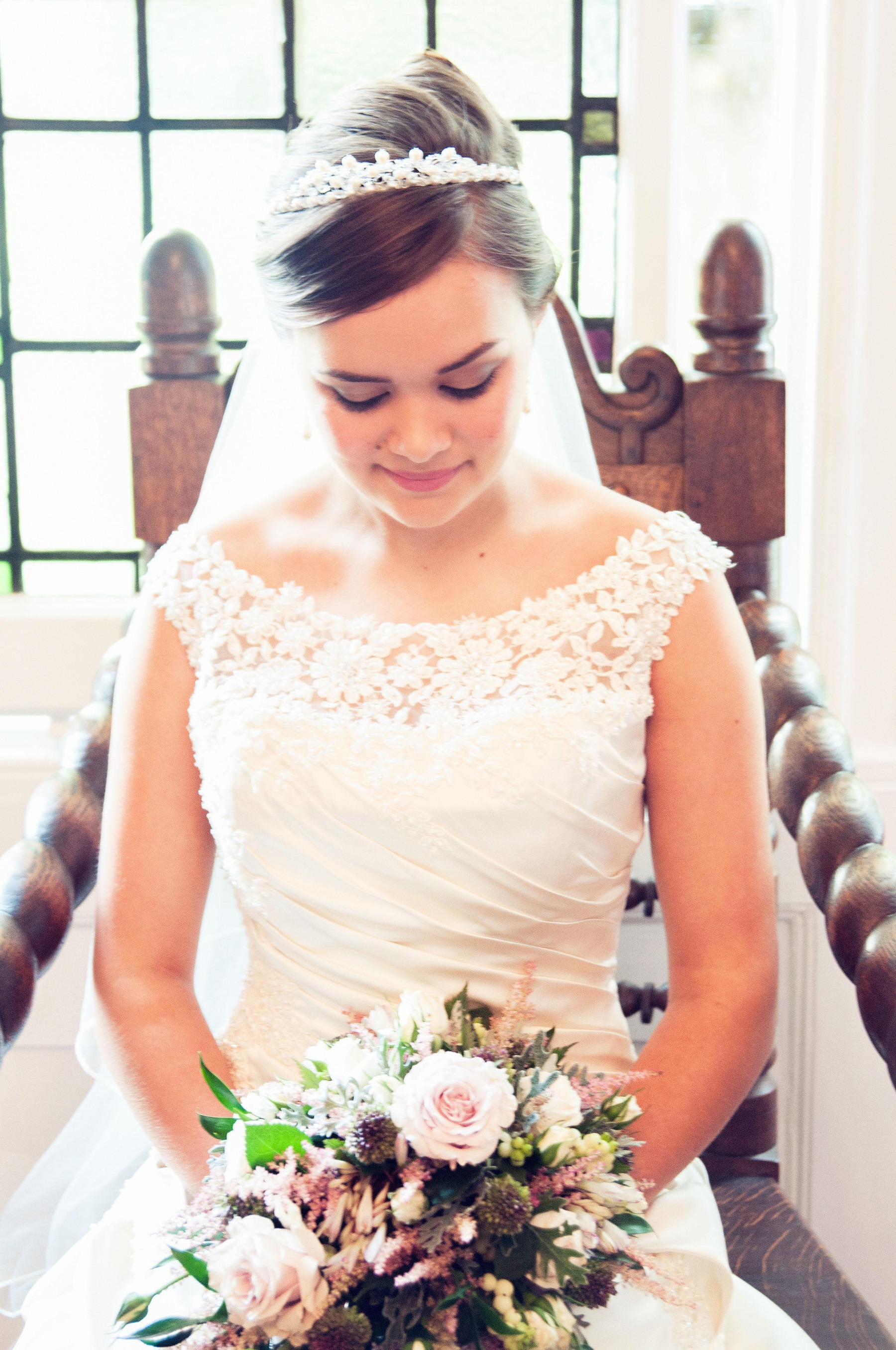 A close up of a bride sitting in the winged chair, holding a bouquet of flowers