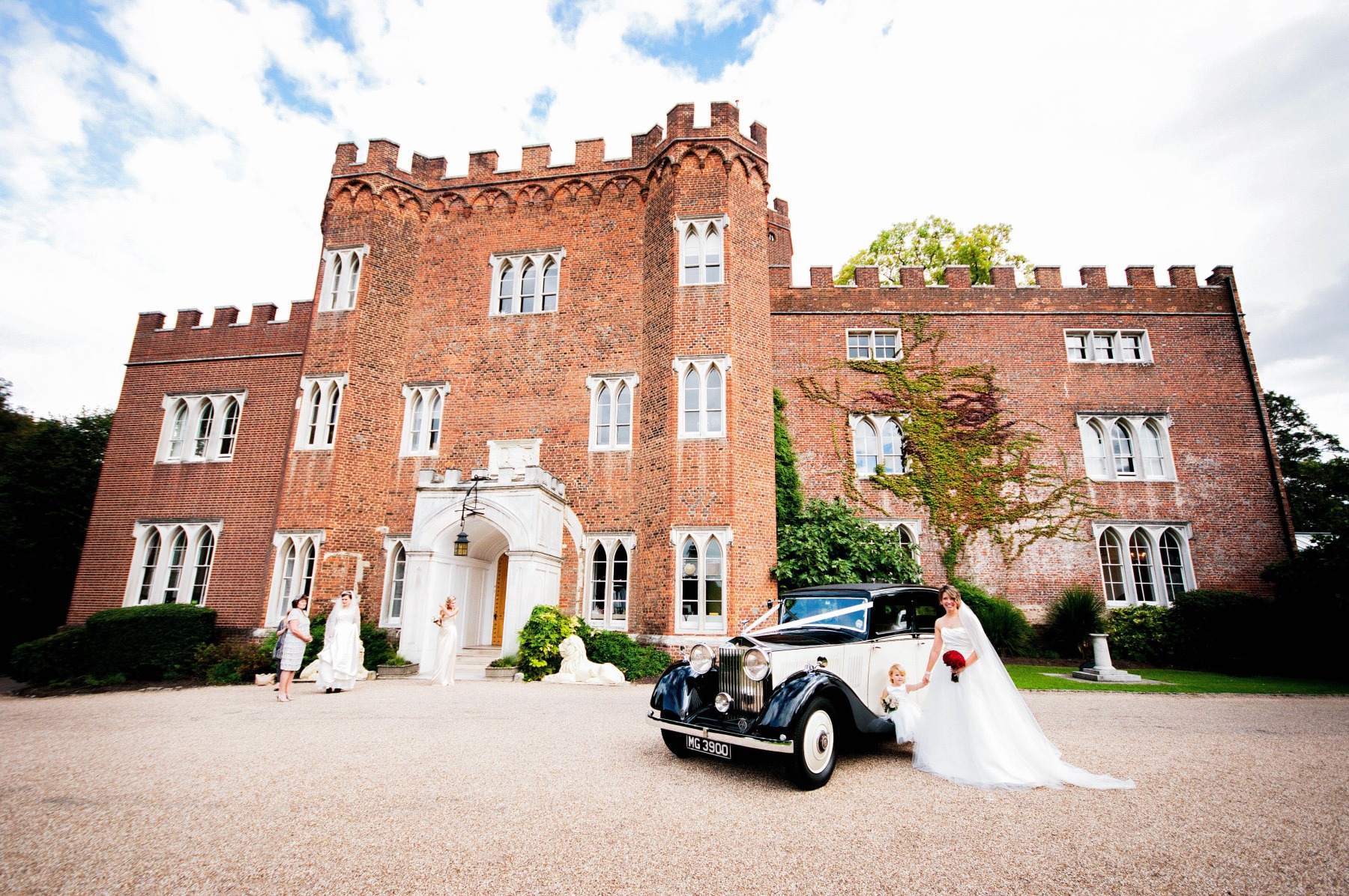 A front full view of Hertford Castle, with a bride and her bridal party by a black and white car