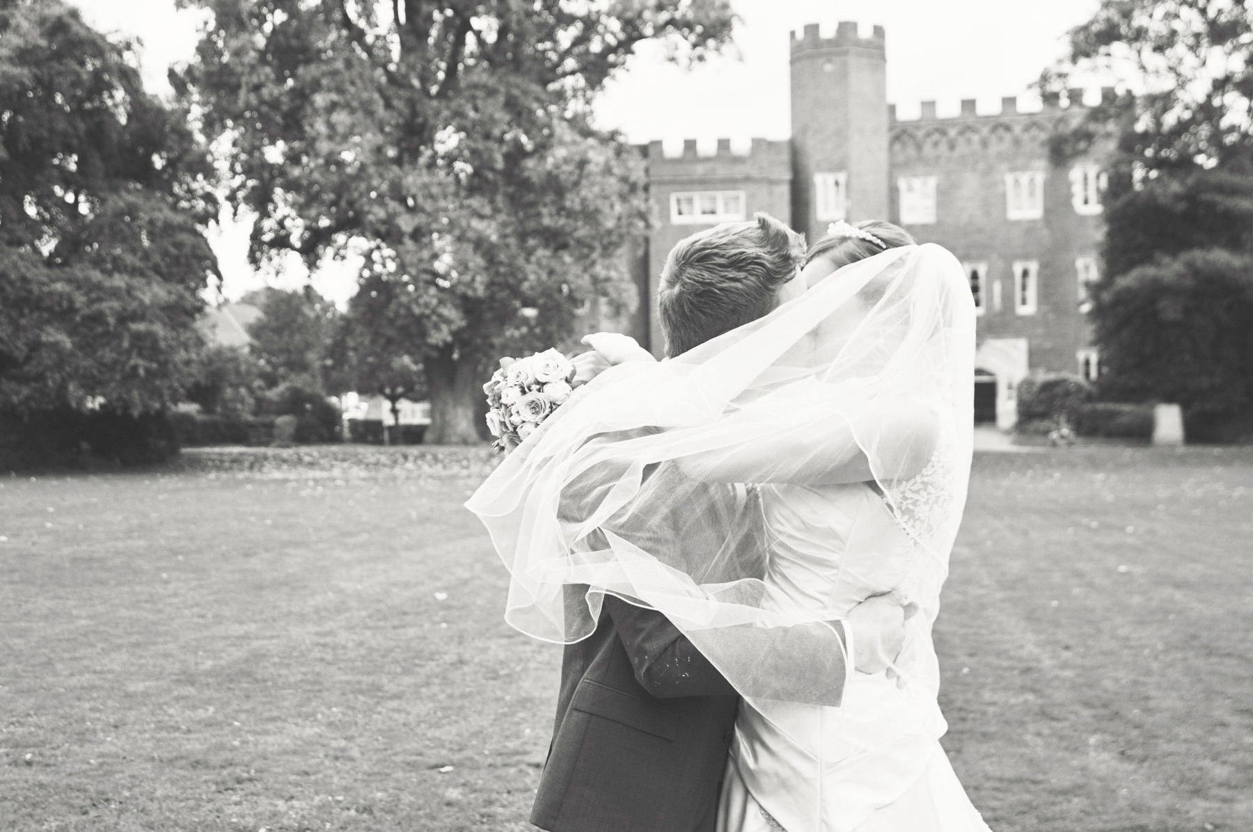 A groom kissing his bride with Hertford Castle in the background, her vail caught in wind
