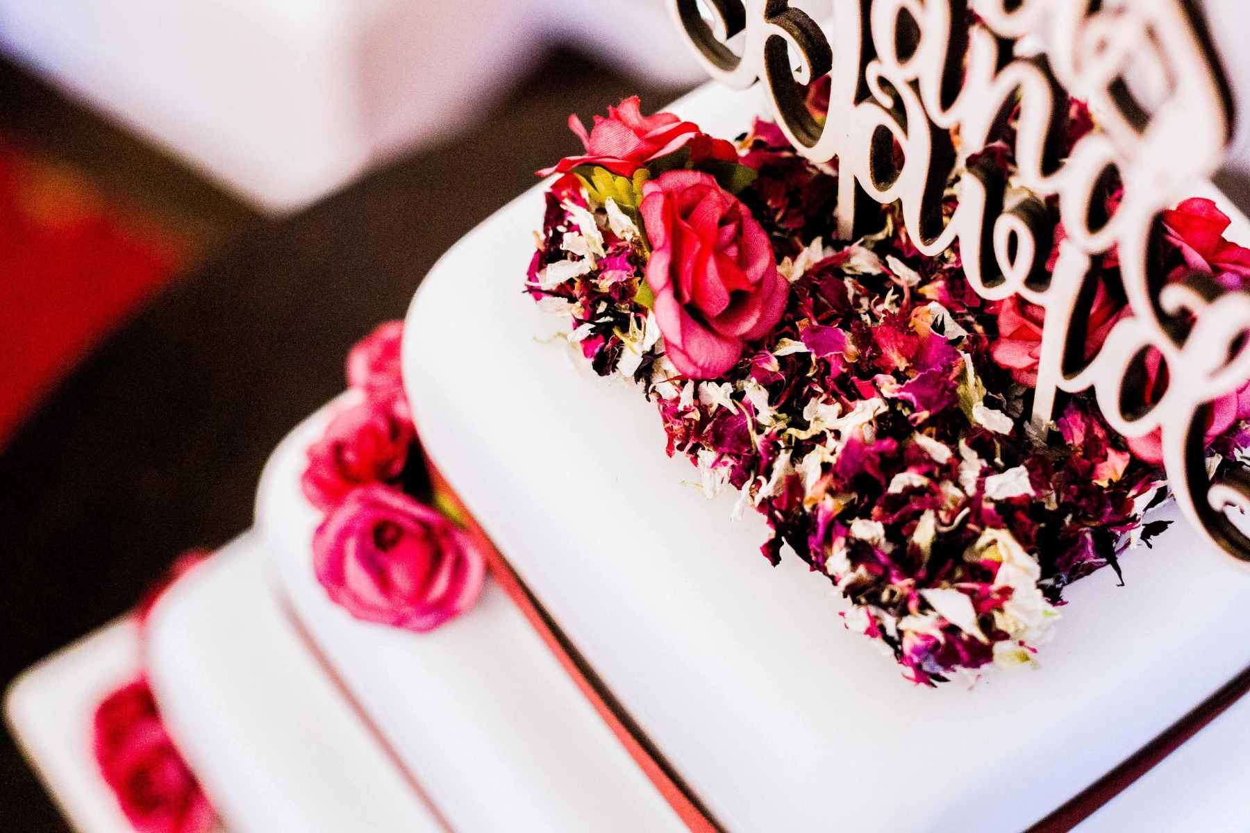 A close up of a white wedding cake with red flowers