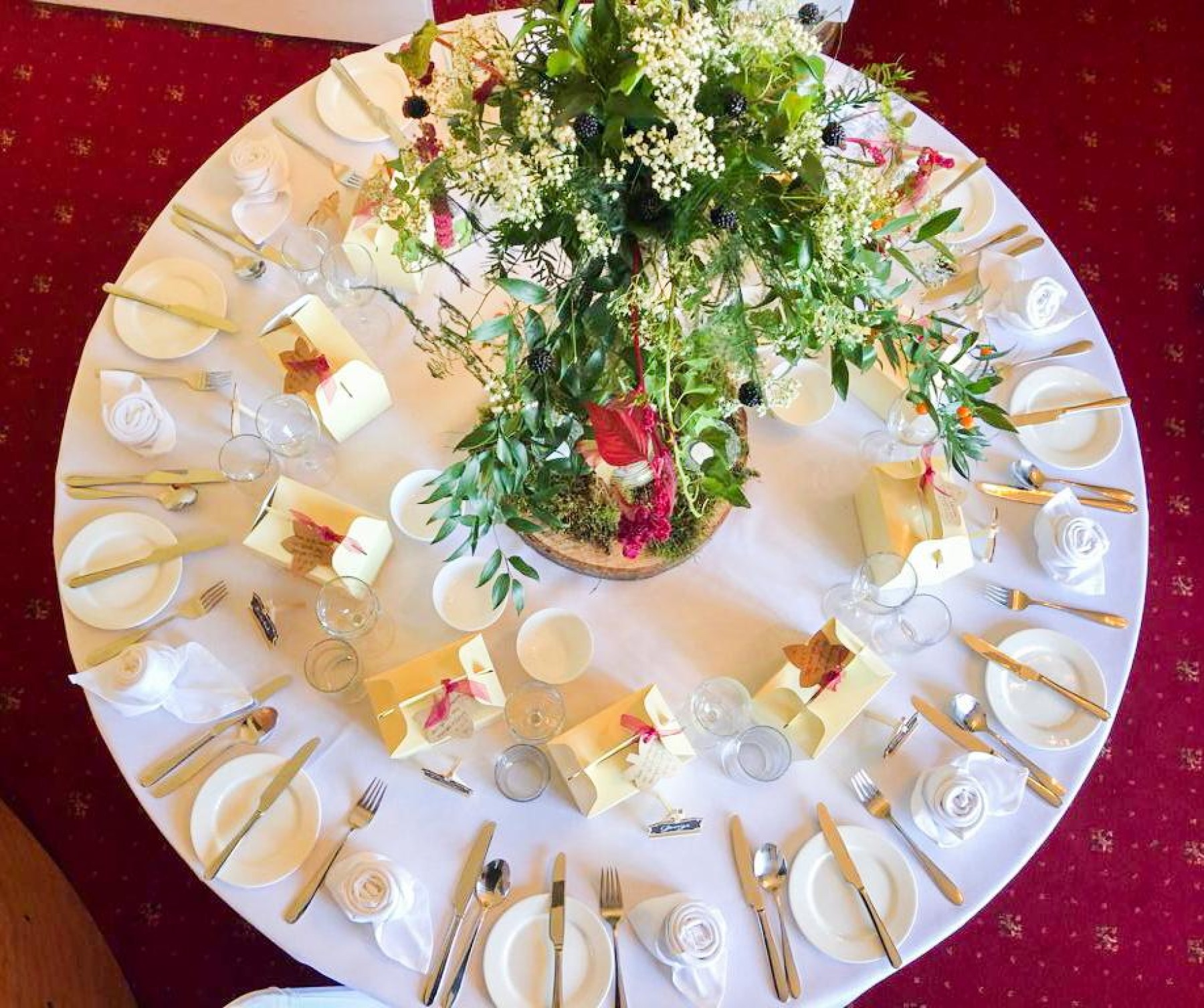 A bird's eye view of a round table dressed and set ready for the wedding breakfast, a huge green floral centrepiece in the middle of the table