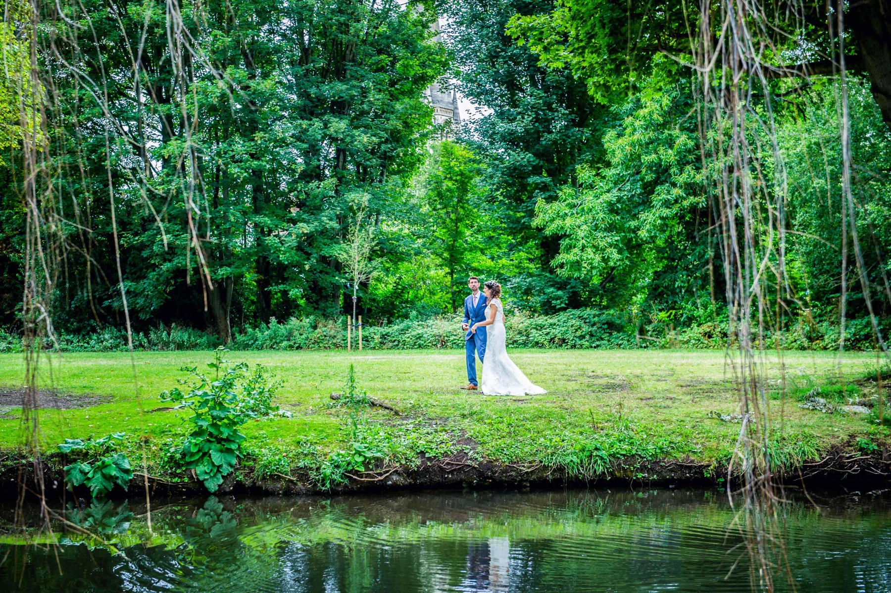 a bride and groom holding hands walking beside the River Lea with the trees surrounding them