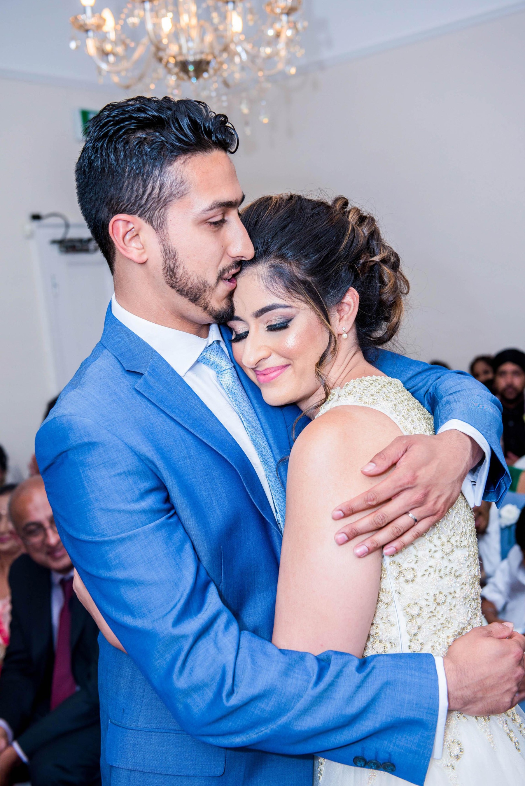 A groom in a bright blue suit cuddling his bride whilse kissing her head