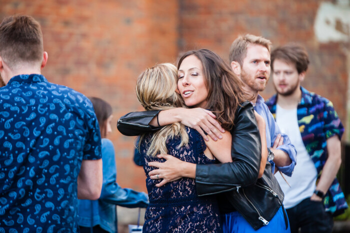 A close up of two woman hugging, whilst smiling with other guests hanging around them in front of the castle. 