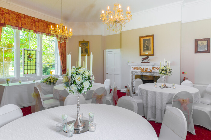 the salisbury room set up for a wedding reception with white table cloths on the round tables, white chair covers and pink box, centrepieces of high f