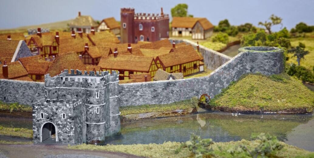 A model of Hertford castle depicting small timber framce houses inside the thick stone curtain wall and gatehouse.