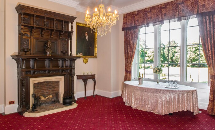 The Mayor's parlour set up with a table in front of the window that looks out onto the main lawn, the ornate wooden fireplace in the centre of the roo