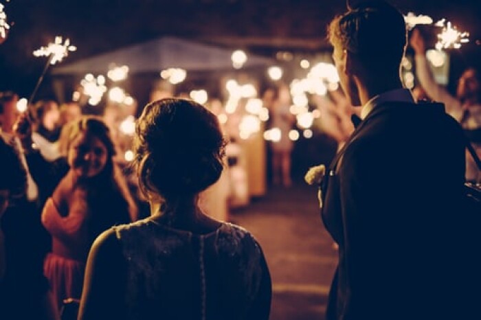 A couple with their back to the camera in silhouette as they walk towards their friends and family waving sparklers