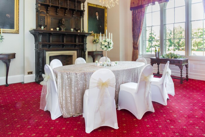 The Mayor's parlour set up for dinner, with the oval table in front of the ornate wooden fireplace covered in a sparkly table cloth and the chairs in 