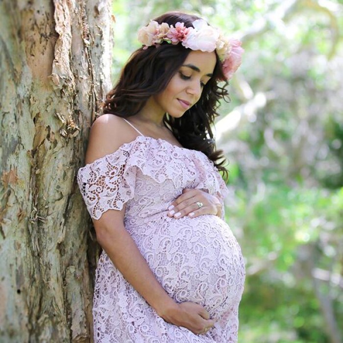 a woman leaning up against a tree clutching her baby bump, clad in a purple lace dress with a flower crown