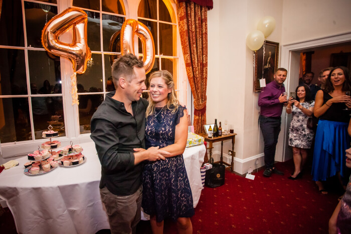 A couple hug in front of a 40 in foil balloons and a table with food on it in the Mayor's Parlour