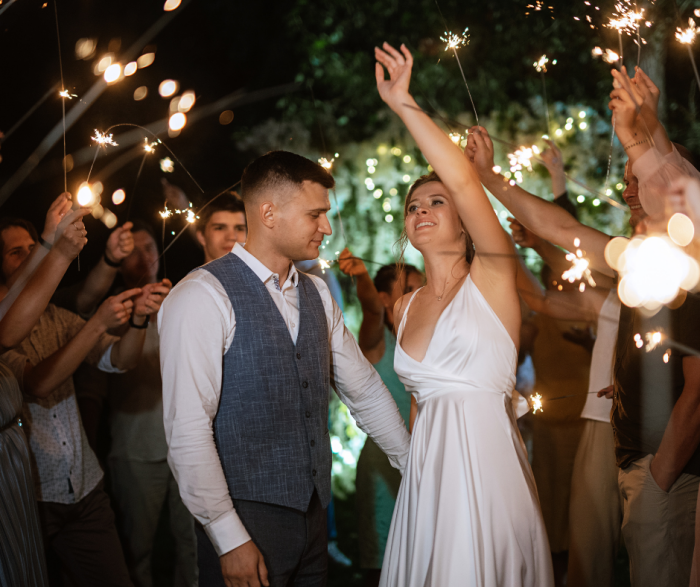 A photo of a bride and groom surrounded by their friends and family waving sparklers