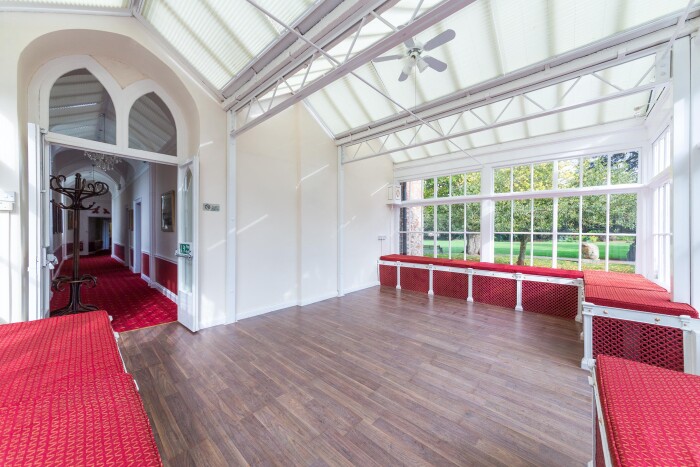 A wide shot of the conservatory, with its white frame, and red cushions on the benches around the edges. 