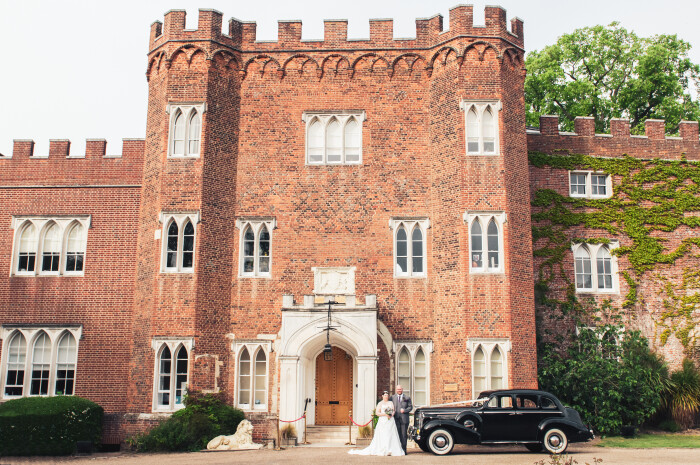 a shot of Hertford Castle from the front, with a bride and groom stood in front beside a black car